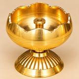 Detailed close-up photograph of a traditional Brass Tamatar Diya showcasing the smooth golden brass interior, raised cylindrical wick holder with a circular opening, rounded tomato-shaped oil bowl, and decorative scalloped flower-petal rim. The polished metal surface displays fine concentric machining marks and horizontal decorative grooves, while the ribbed pedestal base adds traditional detailing. This compact brass oil lamp combines a classic pooja diya design with an elegant golden finish suitable for h