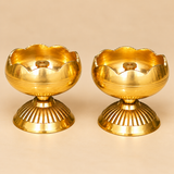 Three-quarter angle photograph of two Brass Tamatar Diyas featuring traditional rounded brass oil bowls with gently curved scalloped rims, polished reflective golden surfaces, fine horizontal decorative grooves, and raised central wick holders. Each diya stands on a beautifully ribbed circular pedestal base that provides a stable foundation. The elegant brass oil lamps are suitable for daily devotional rituals, festive pooja arrangements, home temples, and traditional religious ceremonies.