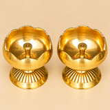 Front perspective of a pair of polished Brass Tamatar Diyas featuring traditional tomato-shaped brass bowls, curved flower-petal rims, engraved horizontal lines around the exterior, and decorative ribbed pedestal bases. The golden brass finish reflects warm light, highlighting the smooth rounded shape and raised centre wick holders. These compact traditional brass oil lamps complement home mandirs, daily prayer arrangements, religious festivals, and ceremonial pooja decorations.