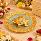 Handcrafted Brass Tortoise Plate shown in a festive devotional setting with diya, flowers and pooja elements, demonstrating its use as a decorative puja item and auspicious home decor accent. The golden tortoise centerpiece and ornamental plate design make it suitable for prayer rooms, festive rituals, vastu-inspired decor, housewarming gifting and traditional celebrations.