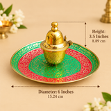 Golden meenakari kumkum box with lid placed on a floral enamel plate, shown as a traditional pooja set on a beige background
