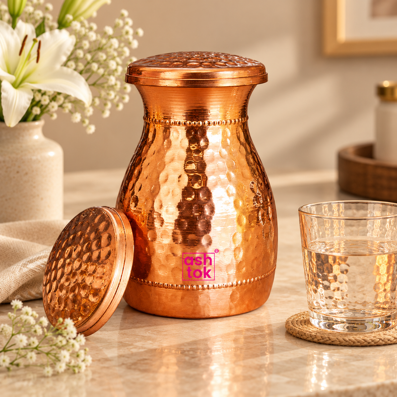 Hammered copper carafe with fitted lid styled in a premium beige home setting beside a drinking glass, showing its use for storing and serving water while highlighting the polished copper finish and traditional handcrafted design.