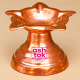 Detailed close-up image of a traditional Copper Diya highlighting its distinctive flower-shaped oil lamp bowl, outward-curving petal edges, polished reddish-copper finish, and decorative pedestal construction. The upper section features a beautifully formed shallow copper bowl surrounded by layered floral extensions with softly pointed edges, giving the diya a unique star-like flower design. The copper surface displays fine handcrafted-style marks, subtle uneven metallic textures, polished highlights, and n