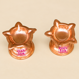 Set of six traditional Copper Diyas displayed together on a premium beige studio background alongside a simple brown cardboard packaging box, illustrating a practical bulk gifting and storage arrangement. The image features six matching flower-shaped copper oil lamps arranged neatly in two rows, with three diyas positioned at the back and three in the foreground. Each copper diya features an elegant shallow bowl surrounded by multiple pointed and curved floral petals, a polished reddish-orange copper finish