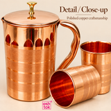 Close-up product image of a polished copper jug with matching copper glasses, showing the smooth fitted lid with decorative knob, curved handle, finely finished copper body, horizontal decorative bands, reflective polished surface and deep copper-toned interior of the drinking glasses, photographed against a clean beige background with ASHTOK branding to highlight the craftsmanship, premium finish, shape, texture and elegant detailing of this copper drinkware set for home use, serving, gifting and festive o