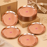 Stacked and displayed round copper plates set next to brown cardboard gift boxes tied with a ribbon.