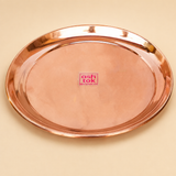 Round polished copper puja plate with a raised rim and Ashtok logo sticker on a beige background.