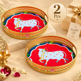 Set of 2 Cow Design Tray Flower Basket and Puja Tray for Temple displayed together in an elegant beige gifting presentation. Each tray features a decorative round shape, golden brass-look finish, intricate cutwork border, vibrant sacred cow artwork and visible ASHTOK logo, making the two-piece set suitable for festive gifting, return gifts, housewarming gifts, religious occasions and puja utility use.