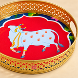 Detailed close-up view of Cow Design Tray Flower Basket and Puja Tray for Temple highlighting the intricate golden cutwork rim, smooth polished brass-look finish, side opening handle detail and vibrant sacred cow artwork in the center. The close-up also shows the ASHTOK logo on the tray, emphasizing the fine decorative craftsmanship and colorful traditional design suitable for puja and temple use.