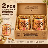 Two piece gift pack of decorative dry fruit gift jar boxes presented together in a premium beige gifting arrangement. Each jar features a polished copper-toned body with intricate floral and leaf-shaped cutwork, a smooth rounded base and a contrasting golden lid topped with a layered flower design and small round knob. The matching pair is suitable for storing dry fruits, almonds, cashews, pistachios, sweets, chocolates, candies and other small festive treats. This 2 piece set is ideal for wedding gifts, ho