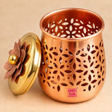 Detailed close-up image of the decorative dry fruit gift jar box shown open on a clean warm beige studio background with the lid placed beside the jar to reveal the interior. The close-up clearly highlights the smooth inner surface, rounded rim, intricate floral and leaf-shaped cutwork pattern across the body and the polished copper-toned finish. 