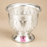 German Silver Gandham Ginni and Sindoor Holder shown from a three-quarter angle on a premium beige studio background, clearly displaying the polished silver-tone finish, broad flared upper rim, rounded decorative bowl, repeating embossed petal motifs, fine dotted texture, tapered lower section and stable pedestal base, photographed with soft neutral reflections to showcase the overall proportions, craftsmanship and traditional styling for storing sindoor, gandham, kumkum or sandal paste during pooja and fes