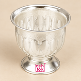Slightly elevated top angle product image of a German Silver Gandham Ginni and Sindoor Holder showing the smooth reflective interior, wide circular rim, decorative embossed outer body and short pedestal base, presented on a premium beige studio background with clean neutral silver reflections, allowing customers to clearly view the interior depth, rim shape, bowl capacity and ornamental detailing for use as a traditional sindoor container, gandham holder, kumkum bowl or pooja accessory.