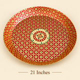 High-angle product shot showcasing an extra-large 21-inch round brass tray decorated with traditional red and gold geometric enamel patterns and green accents, resting on a beige surface with '21 Inches' printed below.