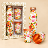 Detailed view of a floral printed copper water bottle and matching drinking glasses showing the smooth polished copper interiors, rounded glass rims, colourful rose-patterned exterior and copper-coloured bottle cap. The close-up highlights the contrast between the white floral decoration and warm copper surfaces.