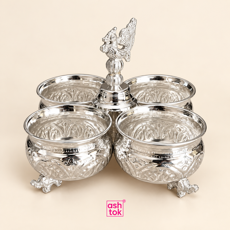 German silver chopala gift item with 4 attached round bowls arranged around a decorative central finial, featuring an elegant embossed surface design, polished silver finish and ornamental raised feet, displayed as a clean studio-style product image on a soft beige background with ASHTOK branding, highlighting its premium traditional appearance and making it suitable for festive gifting, dry fruit serving, table presentation, pooja accessory storage and decorative home use.