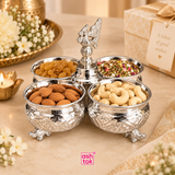 German silver chopala gift item with 4 attached bowls styled in an elegant festive lifestyle setting and filled with assorted serving items such as almonds, cashews, raisins and colorful mouth freshener mix, placed on a beige tabletop with flowers, a diya and a decorative gift box in the background, showing the product as a premium serving and presentation piece suitable for festive hosting, family gatherings, special occasions, table décor, gifting and traditional dry fruit presentation.