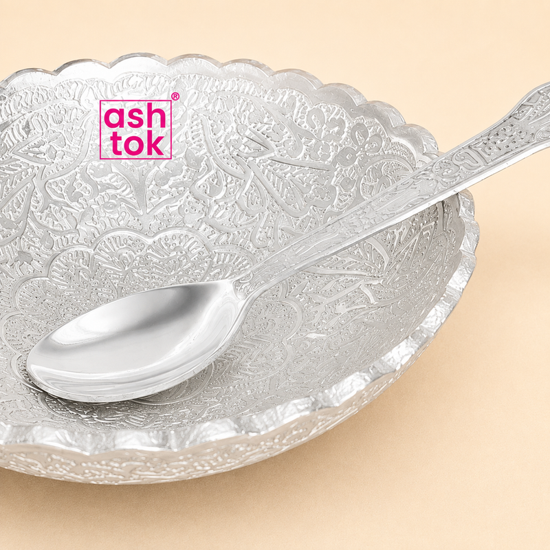Close-up view of a silver-plated decorative gift bowl with detailed floral engravings and a matching engraved spoon.