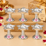Bulk gifting image showing multiple matching German Silver Diyas neatly arranged in a festive setup on a beige and gold styled background with decorative gift boxes, highlighting the polished silver finish, square floral bowl shape, pointed corner details, sturdy pedestal design and coordinated traditional appearance, making the image suitable for wedding return gifts, festive gifting, pooja favors, housewarming gifts, family function giveaways and bulk order presentation.
