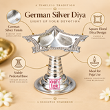 Feature-focused product image of a German Silver Diya on a soft beige background with clean feature callouts, presenting the polished German silver finish, square floral diya design, stable pedestal base and suitability for puja use, while keeping the diya centered and clearly visible with its reflective silver surface, decorative rim details, structured bowl shape and elegant pedestal construction, making it ideal for ecommerce product display and feature explanation.