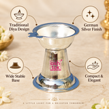 Feature-focused product image of a traditional German Silver Diya displayed on a warm beige background with clean callout icons and feature text, highlighting the traditional diya design, shiny German silver finish, wide stable base and compact elegant form, while showing the product clearly in the center with its shallow bowl, side wick-holder extension, tapered conical body and broad circular base, making it suitable for product pages that explain the design benefits, decorative appeal and devotional util