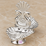 Front angle view of a German Silver Puja Deepam featuring a decorative double swan design rising above two leaf shaped diya bowls, with a polished silver finish and graceful symmetrical structure, photographed on a warm beige background to clearly show the shape, proportions and decorative design for pooja use, home decor and festive gifting.