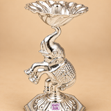 Close-up detail of a German Silver Elephant Pooja Diya highlighting the polished silver surface, facial detailing of the elephant, textured decorative body pattern, curved trunk support, flower shaped diya bowl and embossed pedestal base, photographed on a beige background to emphasize the fine craftsmanship and elegant finish suitable for premium pooja decor and festive gifting.