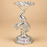 Side view of a German Silver Elephant Pooja Diya showing the raised trunk style support, sculpted elephant body, floral patterned midsection, elevated diya bowl and octagonal pedestal base, photographed on a warm beige background to clearly display the side profile, craftsmanship and decorative form for puja rooms, Diwali decoration, return gifting and housewarming purposes.