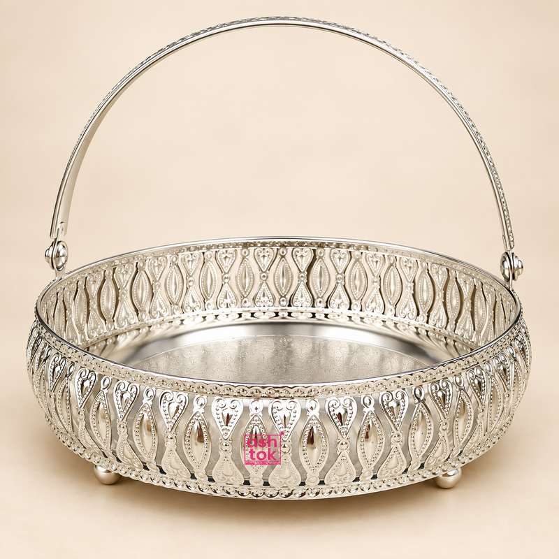 German Silver Flower Butti decorative basket with elegant curved carrying handle, intricate floral and leaf inspired cutwork around the sides, polished silver finish, engraved round base and small raised feet, photographed from the front on a clean beige studio background, suitable for festive gifting, wedding gifts, return gifts, housewarming gifts, pooja accessories, flower presentation, dry fruit arrangement and decorative serving.