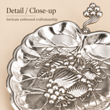 Close-up of German silver gift item showing intricate embossed floral and fruit craftsmanship on a leaf-shaped dish.