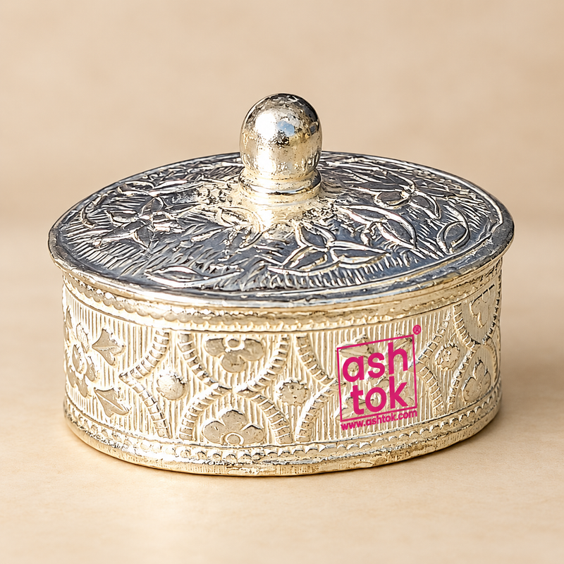 German Silver Kumkum Box shown from a three-quarter angle with intricate floral engraving across the cylindrical body and matching engraved lid, polished silver-tone finish, decorative raised borders and smooth rounded knob, photographed on a soft beige studio background to display the depth, shape, side pattern and traditional craftsmanship of the box for kumkum storage, pooja rituals, festive ceremonies, wedding gifting and decorative use