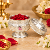 German Silver Kumkum Holder shown open in a warm traditional puja setting with bright red kumkum powder inside, the decorative engraved lid placed beside the container and tasteful flowers and ritual accessories arranged around it, demonstrating practical use for storing and presenting kumkum, roli or sindoor during daily worship, festive puja, wedding ceremonies, religious functions and traditional Indian rituals without any deity idol in the scene.