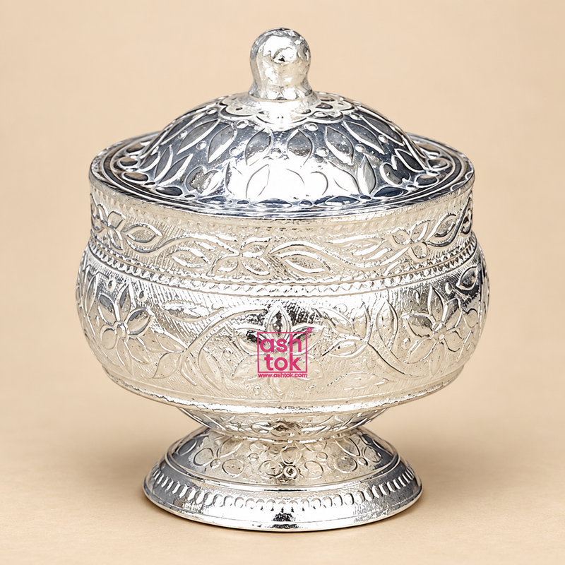 Traditional German Silver Kumkum Holder with a polished reflective silver finish, rounded floral engraved bowl-shaped body, matching domed lid with a small rounded top knob, decorative leaf and flower motifs, detailed border work and a short engraved pedestal base, photographed as a clean front-facing product image on a premium beige studio background, suitable for storing kumkum, roli, sindoor, turmeric and other small pooja essentials for daily worship, festive rituals, wedding ceremonies, home mandir use