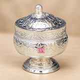 German Silver Kumkum Holder shown from a three-quarter angle on a soft beige studio background, highlighting the rounded engraved body, floral and leaf patterns, polished silver-tone finish, decorative domed lid with top knob, detailed horizontal border bands and short pedestal base, photographed with soft lighting to clearly display the depth, shape, craftsmanship and traditional styling of the kumkum container for pooja use, festive ceremonies, religious rituals and gifting purposes.