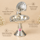 German Silver Peacock Diya featuring an intricately crafted peacock design, bright polished finish, decorative oil lamp bowl, detailed border and stable pedestal base for pooja and festive decoration