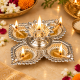 German Silver Pooja Diya displayed in a traditional festive setting with flowers and warm ceremonial lighting, showing four decorative silver diya cups arranged around an ornate flower shaped central holder, suitable for Diwali decoration, daily pooja, festive rituals, home mandir arrangements, religious ceremonies, weddings, housewarming occasions and traditional Indian celebrations.