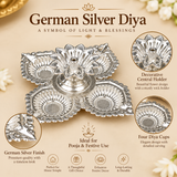 German Silver Pooja Diya features image highlighting the polished silver finish, four individual decorative diya cups, detailed leaf shaped borders, embossed traditional patterns and raised flower shaped central wick holder, designed for pooja ceremonies, festive lighting, Diwali celebrations, home temple decoration, religious functions, traditional gifting and decorative use during Indian festivals.