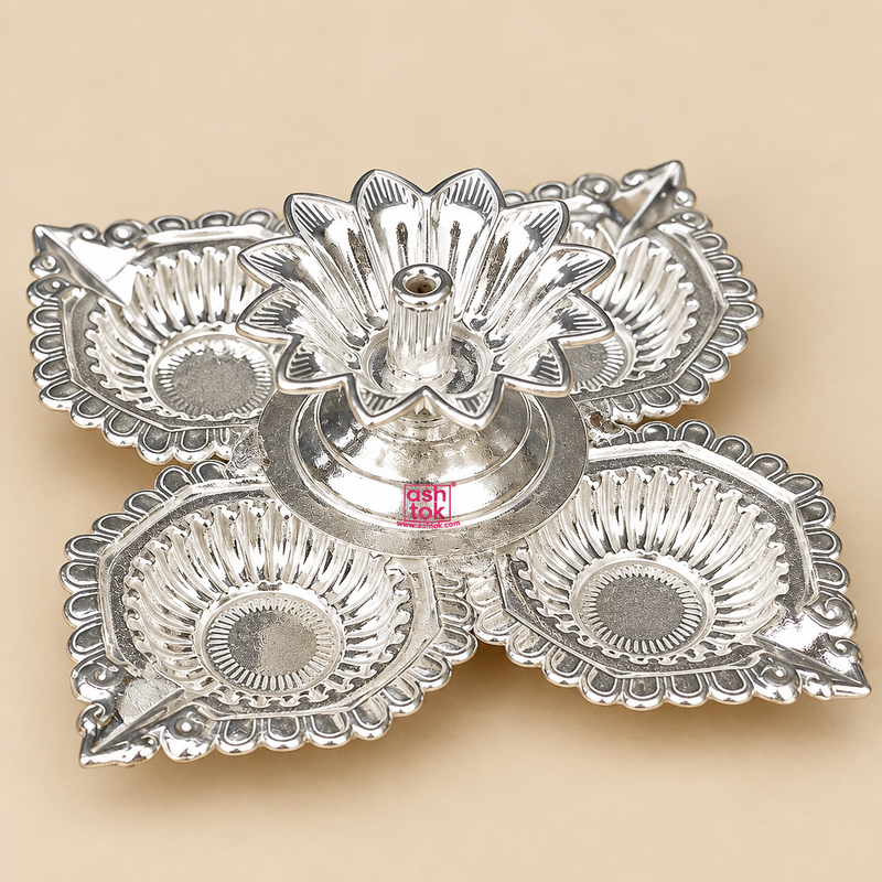 German Silver Pooja Diya with four decorative leaf shaped diya cups arranged around a raised central flower shaped wick holder, featuring an intricate traditional embossed design and bright polished silver finish, photographed on a clean warm beige studio background for Diwali decoration, daily pooja, festive ceremonies, home temple use, housewarming gifts, wedding return gifts and traditional Indian gifting.