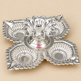 German Silver Pooja Diya with four decorative leaf shaped diya cups arranged around a raised central flower shaped wick holder, featuring an intricate traditional embossed design and bright polished silver finish, photographed on a clean warm beige studio background for Diwali decoration, daily pooja, festive ceremonies, home temple use, housewarming gifts, wedding return gifts and traditional Indian gifting.