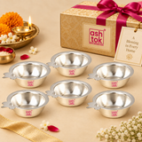 Multiple matching German Silver Puja Diyas arranged neatly in a premium festive gifting presentation with elegant gift box styling, ribbon details, flowers and traditional decorative elements, showing the consistent polished silver finish, shallow round bowl shape, wide rim and side wick-holder tabs, suitable for wedding return gifts, housewarming favors, festive giveaways, pooja gifts, religious functions, family celebrations and larger bulk order requirements.