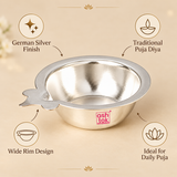 Features image of a German Silver Puja Diya displayed on a warm beige background with elegant callouts highlighting the German silver finish, traditional puja diya design, wide rim design and suitability for daily puja, while keeping the polished round bowl, reflective interior, flared rim and side wick-holder extension clearly visible for customers evaluating the diya for home worship, pooja thali arrangements and festive devotional use.