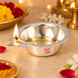 German Silver Puja Diya shown in use in a warm traditional devotional setting with a cotton wick and gentle flame, golden oil or ghee inside the shallow reflective bowl, and tasteful flowers and puja accessories arranged around it, demonstrating practical use for daily worship, evening aarti, Diwali lighting, festive puja, prayer rituals and home mandir ceremonies without any deity idol included in the scene.
