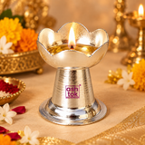 Lit German Silver Puja Diya displayed in a traditional festive pooja setting with flowers, decorative elements and warm ambient lighting, showcasing the lotus petal shaped oil lamp bowl and polished pedestal design for daily worship, Diwali, puja rituals and religious occasions