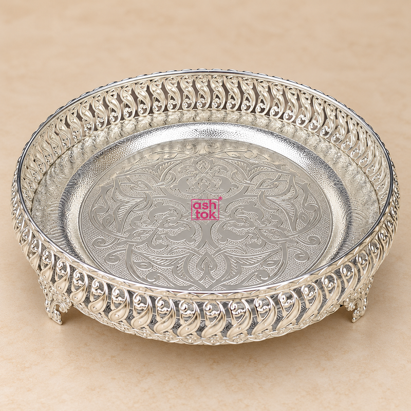 Round German silver puja tray with an intricate engraved floral pattern in the center, decorative openwork border around the rim, and small raised feet at the base. The tray has a polished silver finish with clean neutral reflections and is placed on a soft beige background, showing the full shape and elegant traditional design clearly for product display.