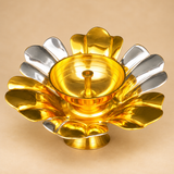 Single gold and silver coated brass lotus diya displayed against a premium beige studio background in a close three-quarter view. The decorative flower-shaped oil lamp features broad alternating golden and silver petals, a polished golden central bowl with a raised wick holder, and a circular pedestal base. This traditional brass diya has a 5.5-inch overall diameter and 2-inch height, making it suitable for home mandir decoration, Diwali pooja, festive arrangements, and traditional gifting.