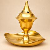Front view of a traditional golden brass agarbati flower incense holder with a tall tapered top, small round smoke ventilation holes, rounded incense chamber and wide leaf-shaped tray at the base, presented on a soft beige studio background to clearly show the polished brass finish, elegant proportions and functional incense-burning design for daily puja and devotional use.
