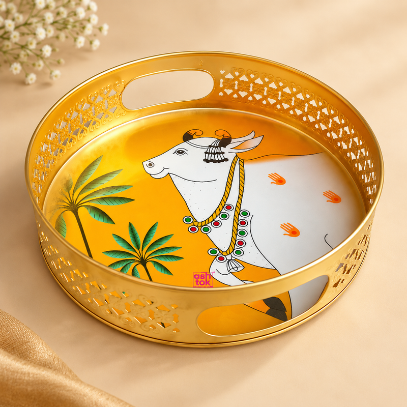 Cow Design Tray Flower Basket and Puja Tray for Temple featuring a round decorative tray with a premium golden finish, intricate cutwork sides, side carry openings and traditional white cow artwork with palm tree motifs on the base. Professionally presented on a clean beige studio background, suitable for puja use, temple offerings, flower presentation, prasad serving, festive rituals and traditional home decor.