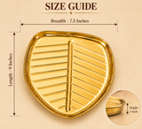 Size guide of a decorative golden leaf-shaped serving tray measuring 9 inches in length, 7.5 inches in breadth and 1 inch in height. The tray features a polished golden metallic finish, raised outer rim, prominent central leaf vein and symmetrical embossed lines extending towards the edges. Its shallow design is suitable for presenting dry fruits, sweets, snacks and festive serving arrangements.