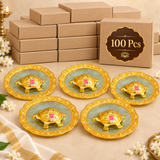 Bulk display of 100 Handcrafted Brass Tortoise Plates presented with plain packaging boxes and selected sample pieces in front on a premium beige background. The product features an ornate golden plate with embossed detailing and a raised brass tortoise centerpiece, making it ideal for large quantity return gifts, housewarming events, festive gifting, wholesalers, bulk orders and traditional gift distribution.