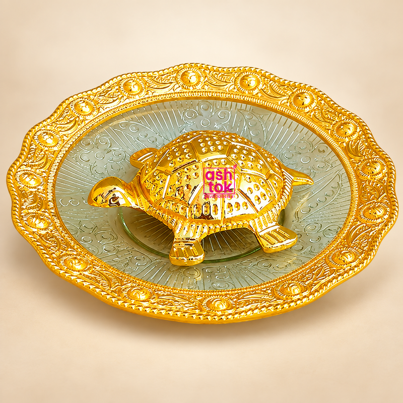 Handcrafted Brass Tortoise Plate displayed on a decorative embossed plate with an ornate scalloped border and rich golden finish, professionally presented on a premium beige studio background. This elegant puja decor item features a detailed brass tortoise placed at the center of the plate and is suitable for housewarming return gifts, festive gifting, traditional decor and auspicious pooja use.